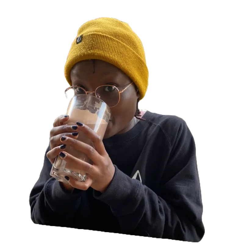 Sonia wearing a yellow beanie and glasses, sipping a drink.
